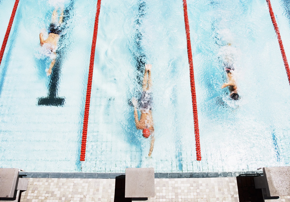 three swimmers about to touch the wall to finish the race