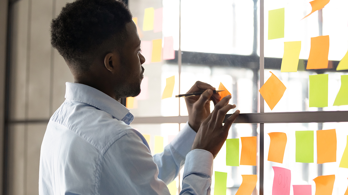 Man writing on and arranging sticky notes on a glass wall