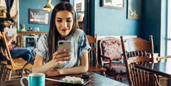 Millennial Generation - young woman checks her phone while enjoing some California rolls at a cafe
